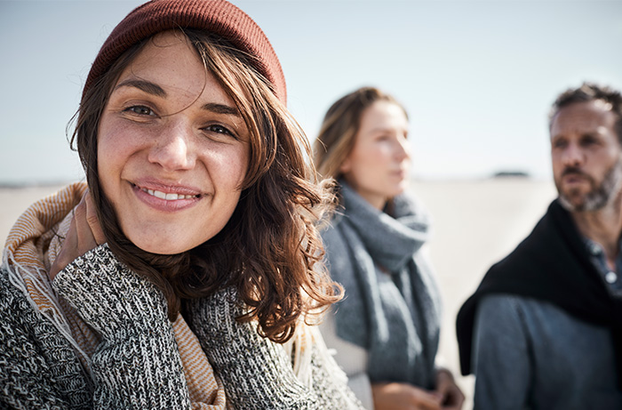 A woman smiling in the camera, two people standing in the background.